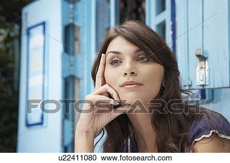 Stock Image - Young woman day dreaming with chin on hand (portrait). Fotosearch