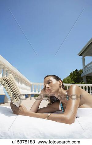Stock Image - Young woman reading book and sunbathing. Fotosearch