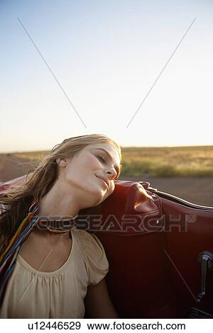 Stock Photo - Young woman with eyes closed traveling in convertible. Fotosearch