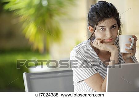 Stock Photo - Young woman with mug using laptop (portrait). Fotosearch