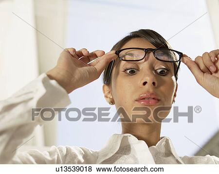 Stock Photo - Young woman lifting eyeglasses (low angle view). Fotosearch