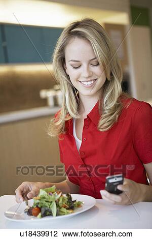 Young woman using cell phone while having lunch View Large Photo Image Stock Image - Young woman using cell phone while having lunch. Fotosearch