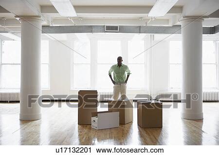 Stock Image - Man standing by cardboard boxes in empty office. Fotosearch
