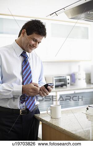 Stock Photograph - Mature man text messaging in kitchen. Fotosearch