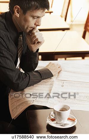 Stock Image - Mid adult man reading newspaper in cafe. Fotosearch