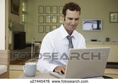 Stock Photo - Mid adult man using laptop in living room. Fotosearch