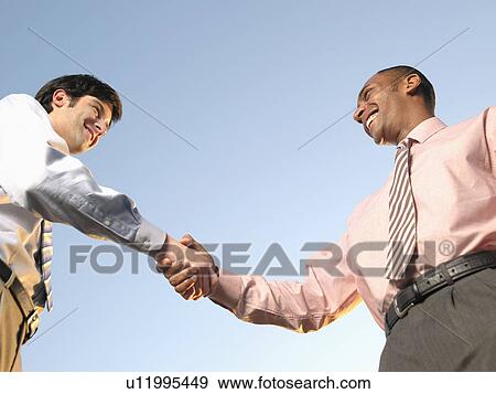 Stock Photo - Two businessmen shaking hands (low angle view). Fotosearch
