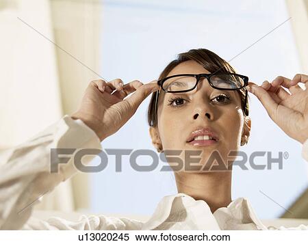 Young woman lifting eyeglasses (low angle view) View Large Photo Image Stock Photography - Young woman lifting eyeglasses (low angle view). Fotosearch