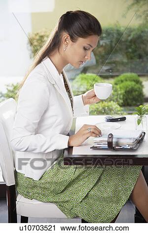 Young woman looking at personal organizer and drinking coffee View Large Photo Image Stock Image - Young woman looking at personal organizer and drinking coffee. Fotosearch