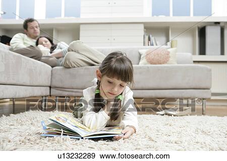 Girl reading book on floor, parents on sofa in background View Large Photo Image Stock Photo - Girl reading book on floor, parents on sofa in background. Fotosearch