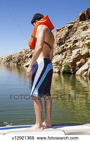 Young man in life jacket standing on motorboat View Large Photo Image Stock Photo - Young man in life jacket standing on motorboat. Fotosearch