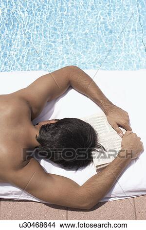Young man sunbathing by pool (high angle view) View Large Photo Image Picture - Young man sunbathing by pool (high angle view). Fotosearch