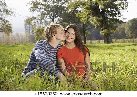 Stock Image - Teenage couple sitting in field. Fotosearch