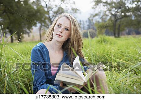 Stock Image - Teenage girl reading book in field. Fotosearch