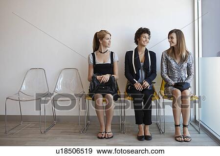 Stock Photo - Three teenage girls sitting on chairs in lobby. Fotosearch