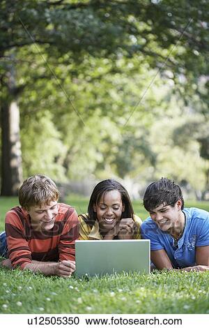Stock Image - Three teenagers using laptop in park. Fotosearch