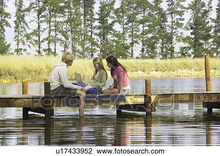 Three teenagers using laptop on jetty View Large Photo Image Stock Image - Three teenagers using laptop on jetty. Fotosearch
