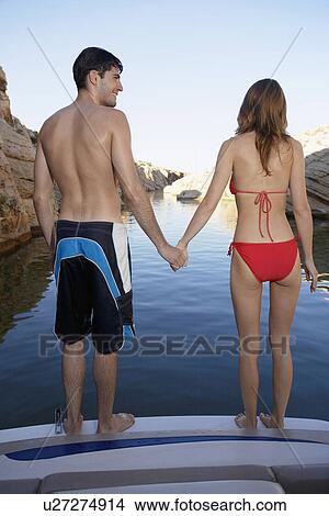 Picture - Young couple holding hands at the edge of motorboat. Fotosearch