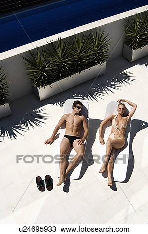 Stock Image - Young Couple Sunbathing on Lounge Chairs. Fotosearch