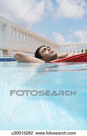Young man lying on air mattress in swimming pool (surface level) View Large Photo Image Stock Image - Young man lying on air mattress in swimming pool (surface level). Fotosearch