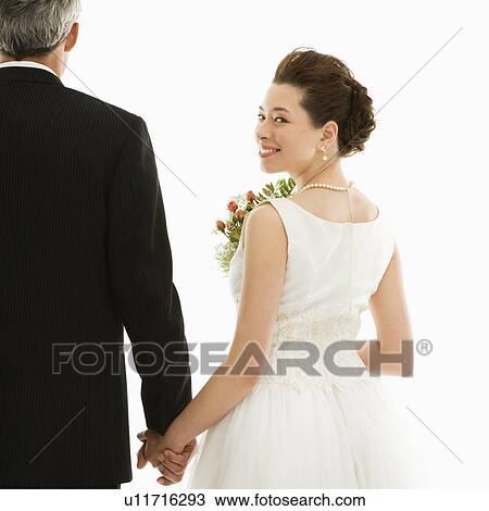 Stock Image - Bride looking over her shoulder while holding groom's hand. Fotosearch