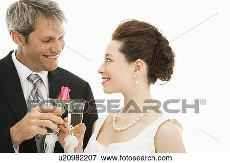 Stock Photo - Caucasian groom and Asian bride toasting with champagne glasses.. Fotosearch