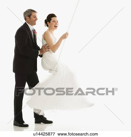 Stock Photo - Caucasian groom pushing Asian bride in swing set.. Fotosearch