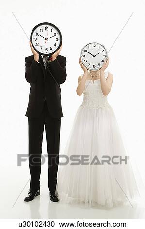 Stock Image - Groom and bride with clocks covering their faces. Fotosearch