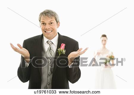Stock Image - Groom in foreground with hands raised in air and bride in background. Fotosearch