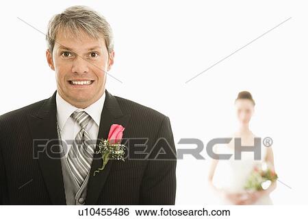 Stock Photograph - Groom in foreground with scared expression and bride in background. Fotosearch