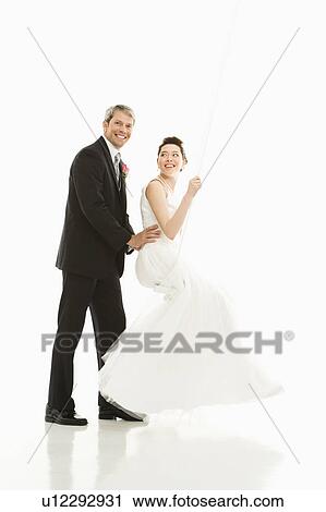 Stock Image - Groom pushing bride in swing. Fotosearch