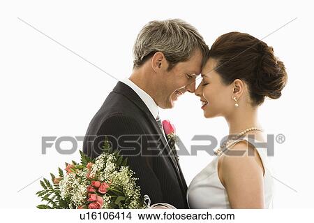 Picture - Portrait of Caucasian groom and Asian bride embracing. Fotosearch
