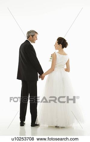 Stock Photo - Portrait of Caucasian groom and Asian bride holding hands. . Fotosearch