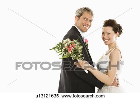 Stock Photography - Portrait of Caucasian groom and Asian bride embracing.. Fotosearch