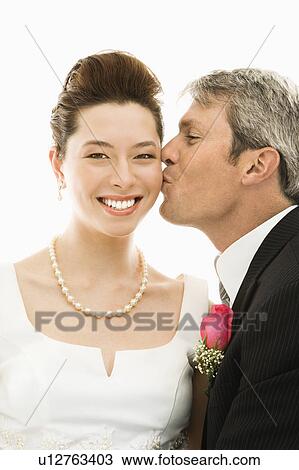 Stock Image - Portrait of Caucasian groom kissing Asian bride.. Fotosearch