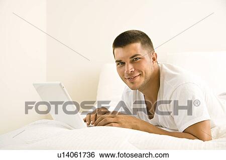 Adult man lying in bed with laptop looking at camera View Large Photo Image Stock Photograph - Adult man lying in bed with laptop looking at camera. Fotosearch