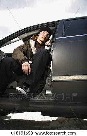 Stock Photo - Confident male teenager sitting in car. Fotosearch