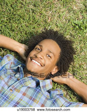 Lying in grass smiling with hands behind head View Large Photo Image Stock Photo - Lying in grass smiling with hands behind head. Fotosearch
