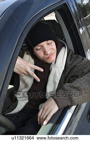 Picture - Male teenager making hand gesture while sitting in car. Fotosearch