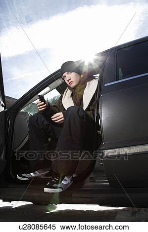 Male teenager sitting in car holding his cell phone. View Large Photo Image Stock Photography - Male teenager sitting in car holding his cell phone.. Fotosearch