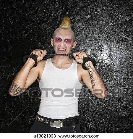 Stock Image - Mid-adult male punk pulling chain between handcuffs.. Fotosearch