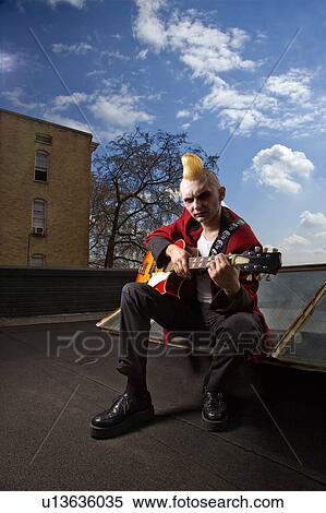 Portrait of a mid-adult male punk sitting on a skylight playing guitar View Large Photo Image Stock Photography - Portrait of a mid-adult male punk sitting on a skylight playing guitar. Fotosearch