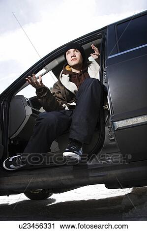 Stock Image - Teenager sitting in car making hand gesture. Fotosearch