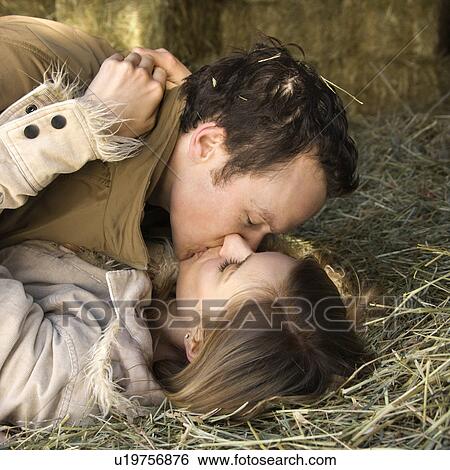Stock Photograph - Couple lying down in hay kissing. Fotosearch