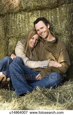 Stock Photo - Couple sitting on hay hugging. Fotosearch