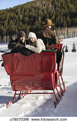 Stock Photograph - man driving horse drawn sleigh with young couple looking back. Fotosearch