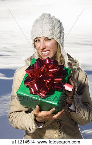 Picture - Woman outdoors in winter attire holding present. Fotosearch