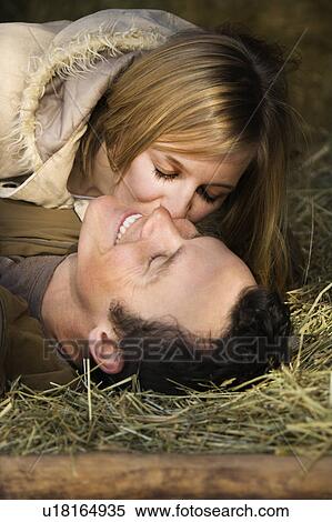 Stock Photography - Young adult woman kissing boyfriend while lying in hay. Fotosearch