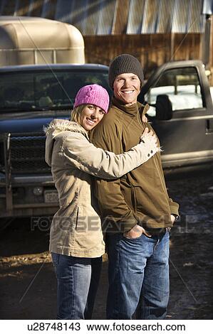 Stock Image - Young Caucasian couple embracing with truck in background.. Fotosearch