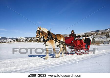 Stock Image - Young couple and mid adult man on horse drawn sleigh ride through winter landscape.. Fotosearch